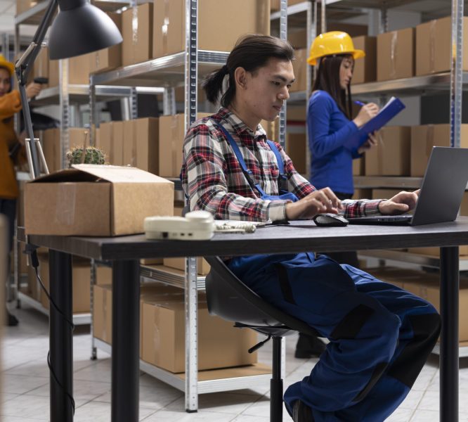 Asian staff member in a local brand supply room prepares products and taped boxes for shipment. Small business activity uses in house logistics for storage and delivery services.